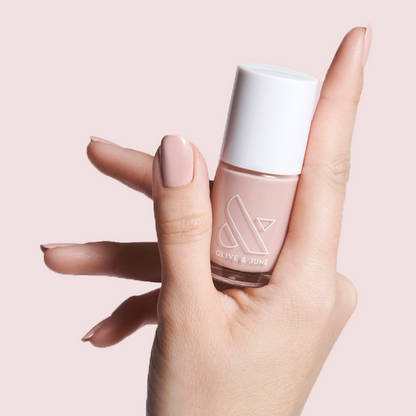 Hand holding Olive and June bottle with nails polished in HZ rosy neutral shade on light pink background