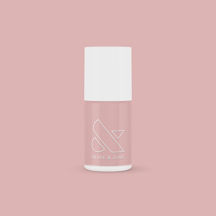 HZ nail polish bottle by Olive and June in a soft rosy neutral shade on a muted pink background