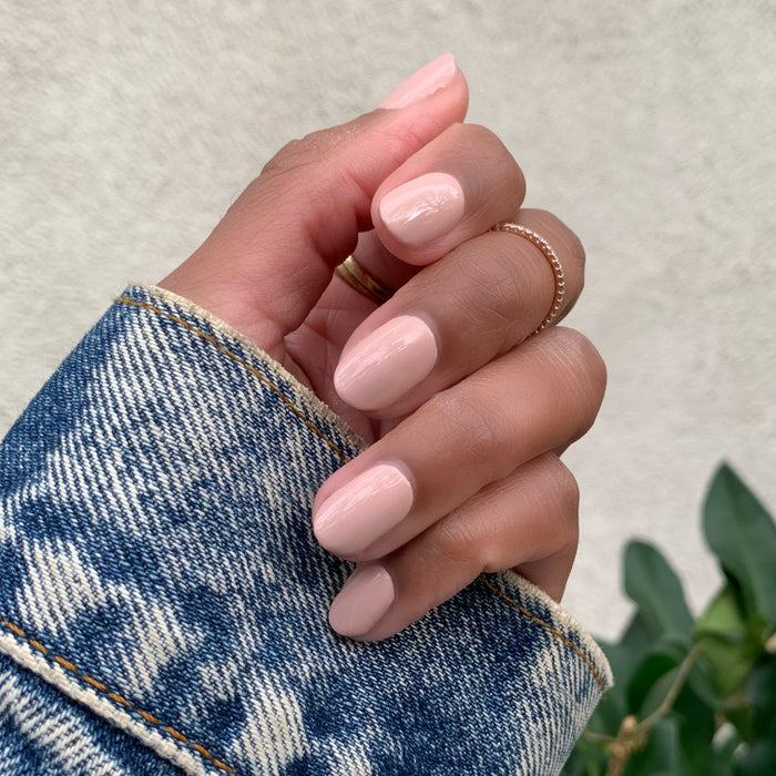 Hand with nails polished in HZ showing a soft rosy neutral manicure with a natural glossy finish against denim sleeve