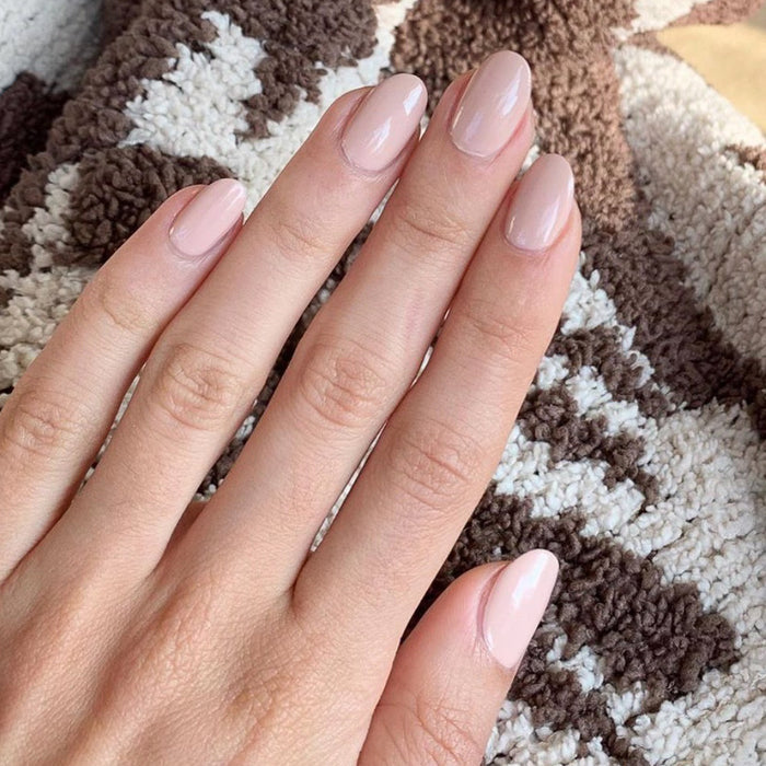 Hand with nails polished in HZ showing a glossy rosy neutral manicure on a textured brown and white surface