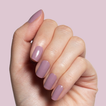 Hand with glossy midtone mauve manicure painted with I Mani in Meetings polish against soft lavender background