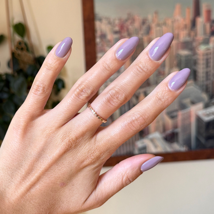 Hand with glossy purple midtone mauve manicure using I Mani in Meetings polish against soft cityscape background