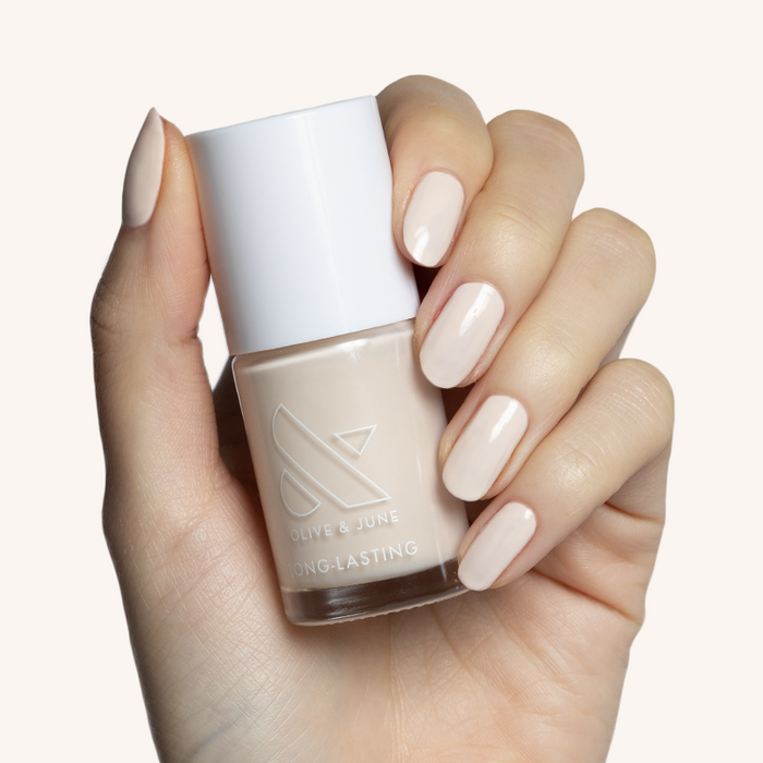 Hand holding a bottle of It's Chilly! long-lasting neutral beige nail polish with matching painted nails.