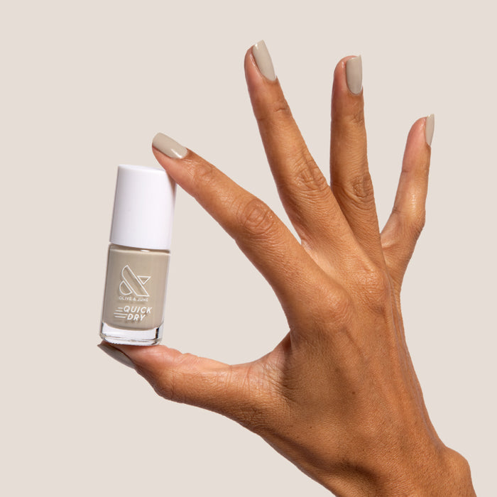 Hand holding Koala nail polish bottle with nails painted in soft grey shade against a light background