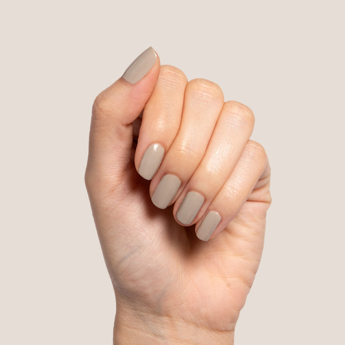 Hand with nails polished in Koala soft grey shade showing a smooth, cozy manicure on neutral beige background