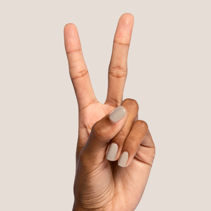 Hand with nails polished in neutral Koala soft grey shade making a peace sign on a beige background