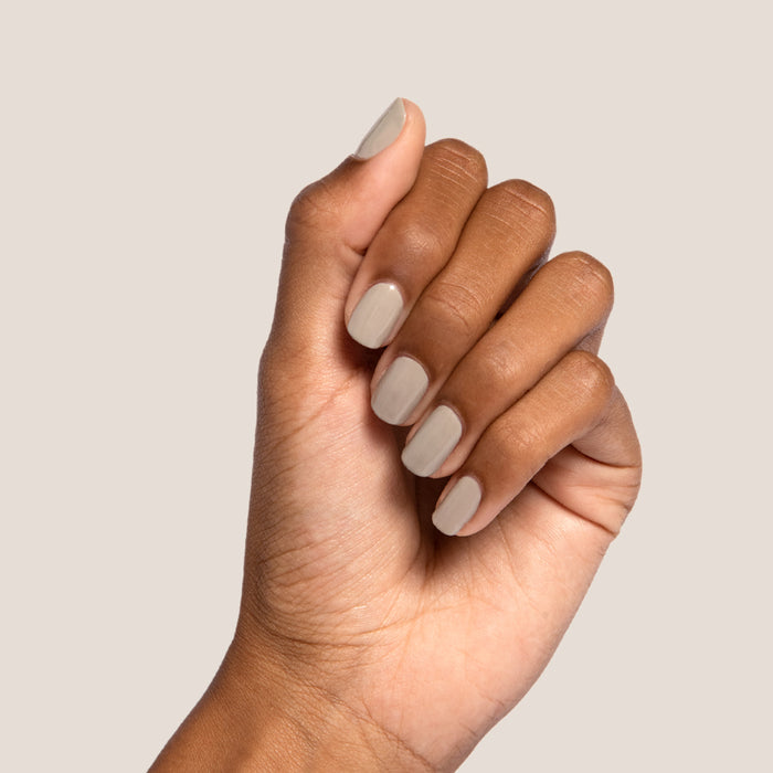 Hand with nails polished in Koala soft grey shade showing a smooth manicure on a light beige background