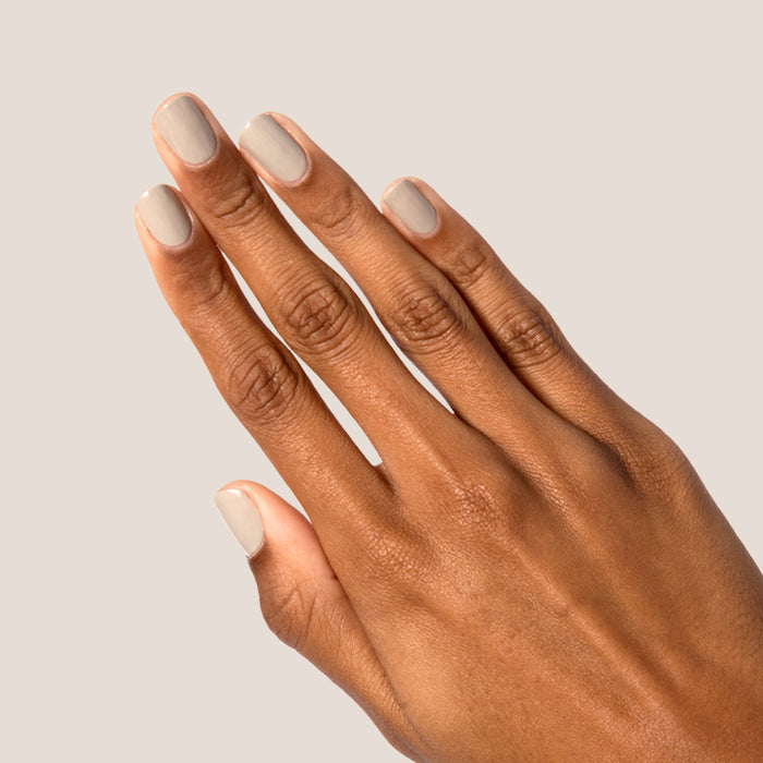 Hand with nails polished in Koala soft grey shade showing a neat manicure on a pale beige background