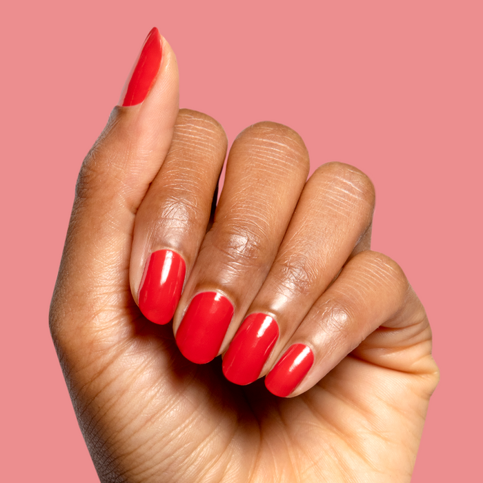 Hand with glossy bright orange red Let’s Circle Back gel polish manicure on a solid soft pink background