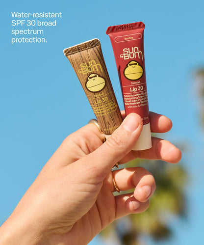Hand holding Sun Bum Lip 30 Duo: Clear + Bonfire tubes against blue sky showing water-resistant SPF 30 protection. Water-resistant
SPF 30 broad spectrum protection.
