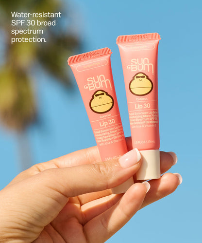 Hand holding two Sun Bum Lip 30 Duo: Sunset Cove + Sunset Cove tubes with blue sky background and product benefits text. Water-resistant
SPF 30 broad spectrum protection.