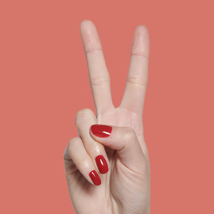 Hand showing peace sign with nails painted in deep red Lipstick Stain long-lasting polish against muted coral backdrop