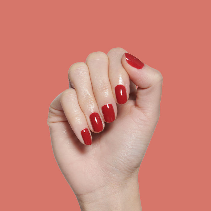Hand with short rounded nails painted in glossy Lipstick Stain deep berry long-lasting polish against coral background