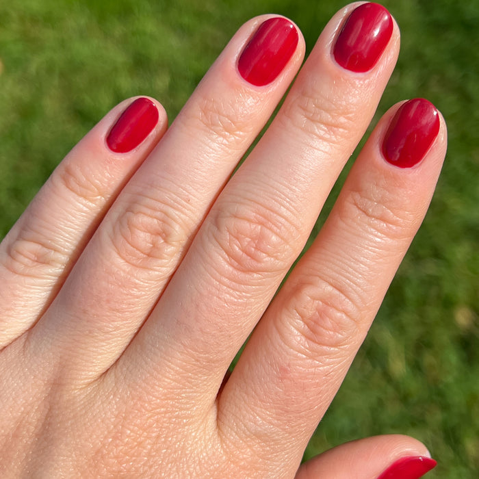 Hand with short rounded nails painted in glossy Lipstick Stain deep berry red polish outdoors on a sunny day