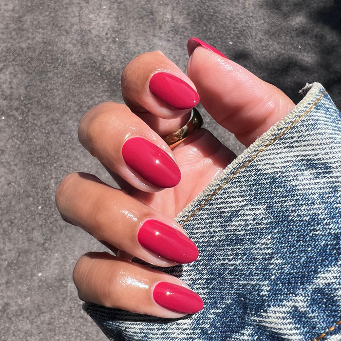 Hand with almond-shaped nails in glossy Lipstick Stain polish holding denim jacket sleeve outdoors in sunlight