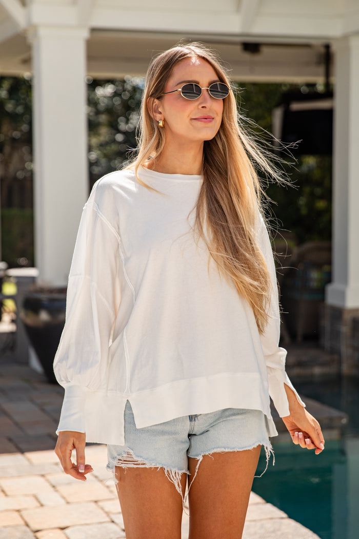 Woman wearing a white blouse and denim shorts by a poolside.