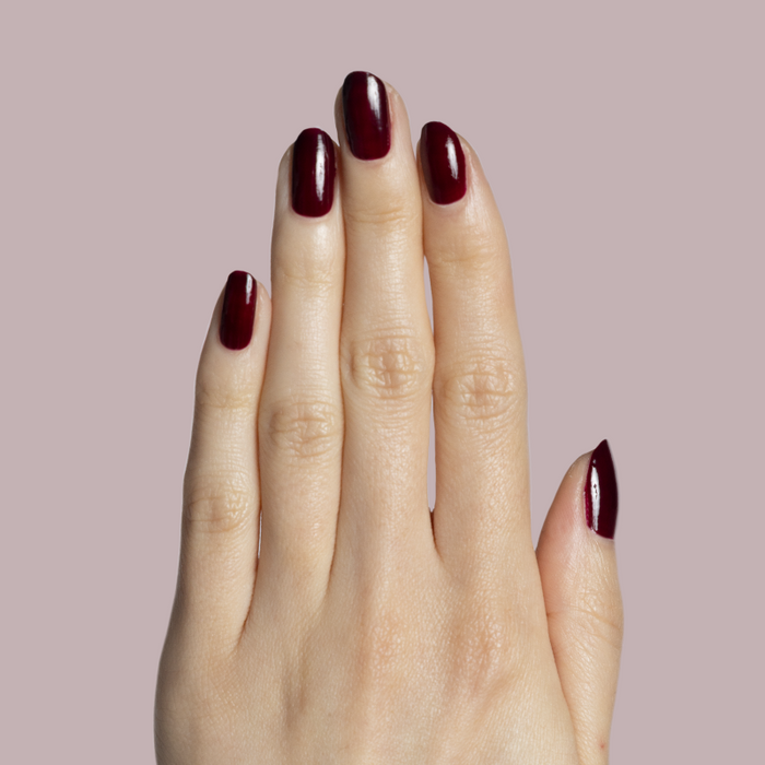 Hand with fair skin wearing Luxe Loafer gel polish in deep crimson jelly for a glossy, patent leather effect manicure