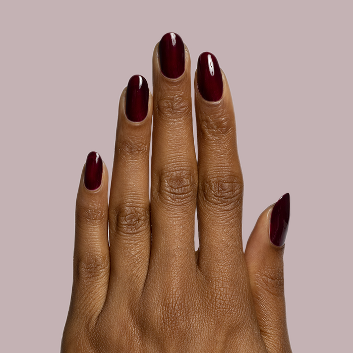 Hand with medium dark skin tone wearing Luxe Loafer glossy deep crimson gel polish manicure on muted mauve background