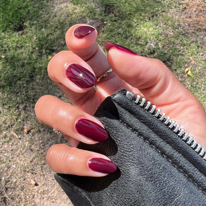 Hand with medium skin tone wearing Luxe Loafer gel polish in glossy crimson jelly shade outdoors with black leather jacket