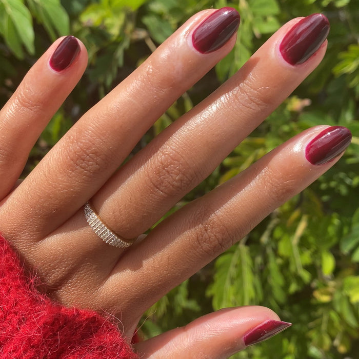 Hand with medium skin tone wearing Luxe Loafer gel polish in deep crimson jelly for a glossy, long-lasting manicure outdoors