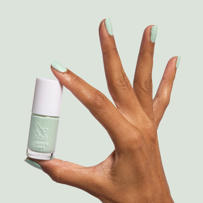 Hand with nails painted in pastel mint green holding a bottle of Minty quick dry polish for an easy at-home manicure