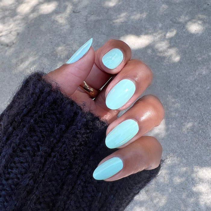 Hand with nails painted in pastel mint green Minty polish showing a fresh, glossy at-home manicure by Olive and June