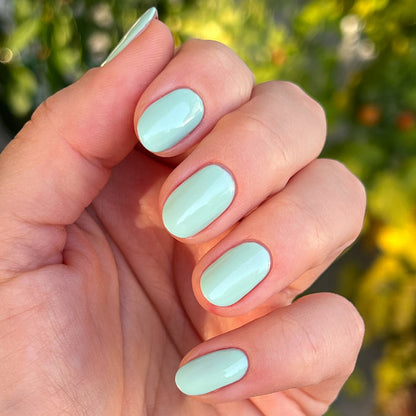 Hand with nails coated in glossy pastel green Minty polish for a fresh, at-home manicure by Olive and June