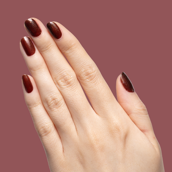 Hand with medium-length nails painted deep shimmery brown Museum Date gel polish against mauve background