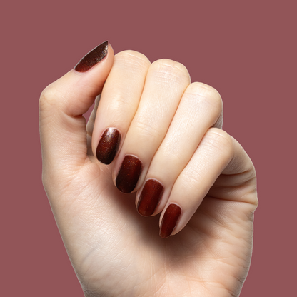 Hand with medium-length nails painted deep shimmery Museum Date gel polish against muted warm mauve background