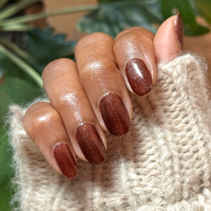 Hand with oval nails painted deep shimmery chocolate brown Museum Date gel polish wearing cozy knit sleeve indoors