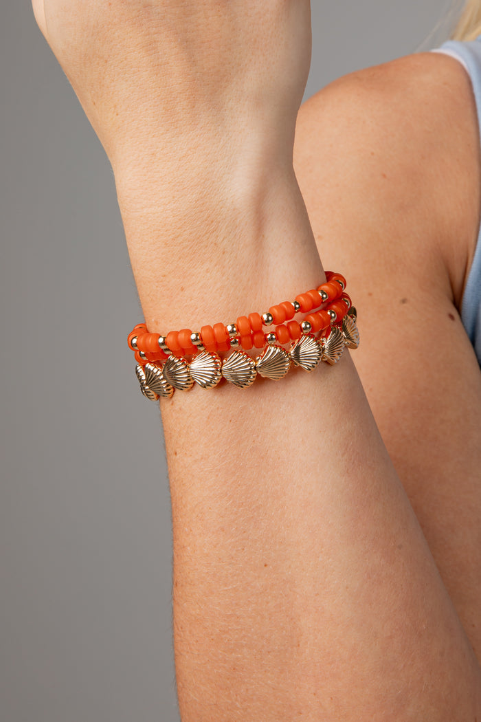 Close-up of a person's arm wearing an orange beaded bracelet with gold accents on a gray background