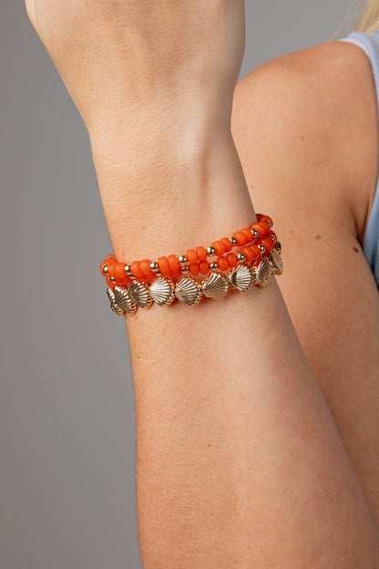 Close-up of a person's arm wearing an orange beaded bracelet with gold accents on a gray background