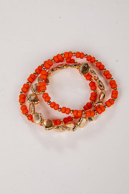 Set of orange beaded bracelets with gold accents on a light gray background