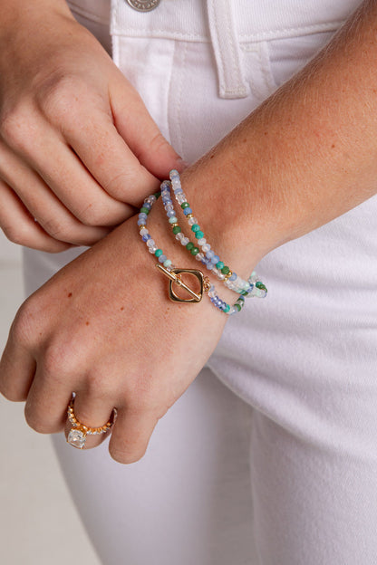 Close-up of a person wearing a beaded bracelet and ring on a plain background