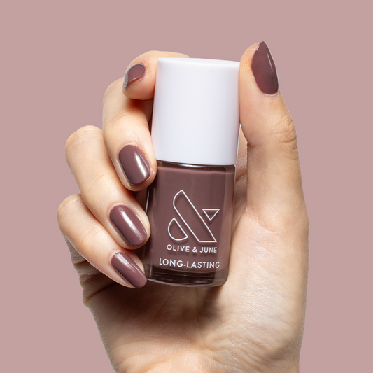 Hand holding Olive and June Patron of the Arts long-lasting gel polish with dusty rose brown manicure against mauve background