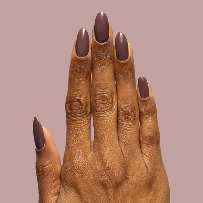 Hand with almond-shaped nails painted dusty deep rose brown Patron of the Arts gel polish against muted mauve background