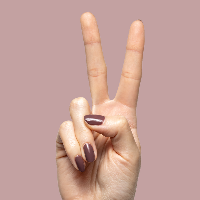 Hand showing peace sign with nails coated in dusty deep rose brown Patron of the Arts gel polish against mauve backdrop
