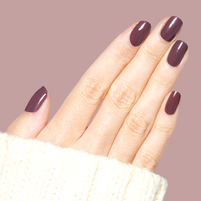 Hand with medium-length nails coated in Patron of the Arts dusty deep rose brown gel polish against soft mauve background