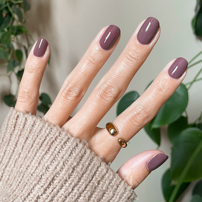 Hand with shiny nails painted in Patron of the Arts dusty deep rose brown gel polish wearing cozy beige sweater indoors