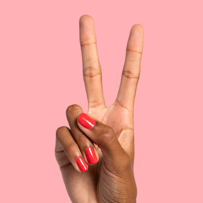 Hand showing peace sign with nails painted in bright orangey red Picante polish on smooth pink background for mani display