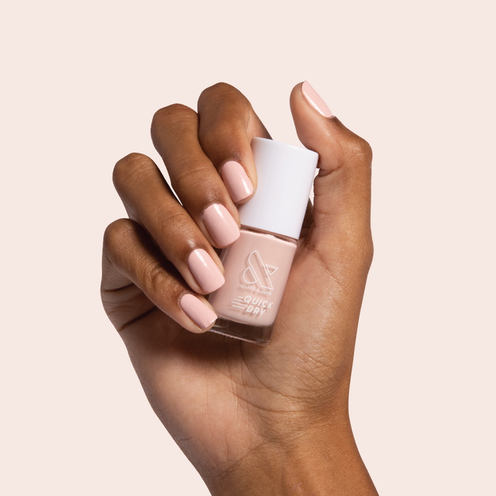 Hand holding a bottle of Pointe nail polish with matching soft pink manicure for an elegant at-home mani look