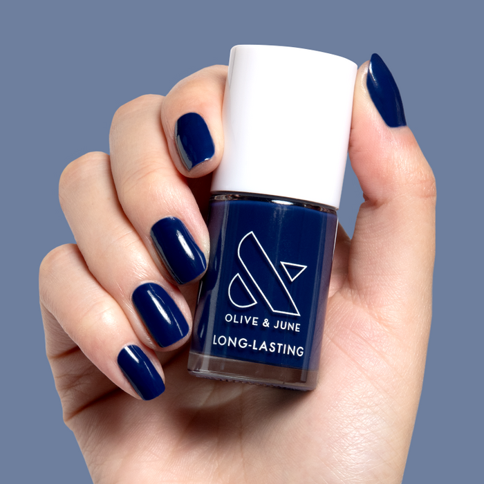 Hand holding Power Suit nail polish bottle with matching deep navy blue long-lasting manicure on nails