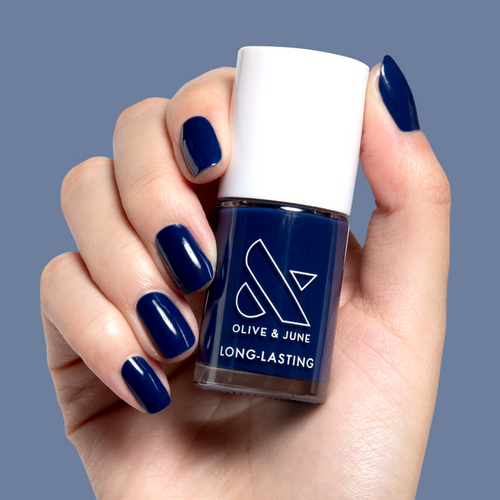 Hand holding Power Suit nail polish bottle with matching deep navy blue long-lasting manicure on nails