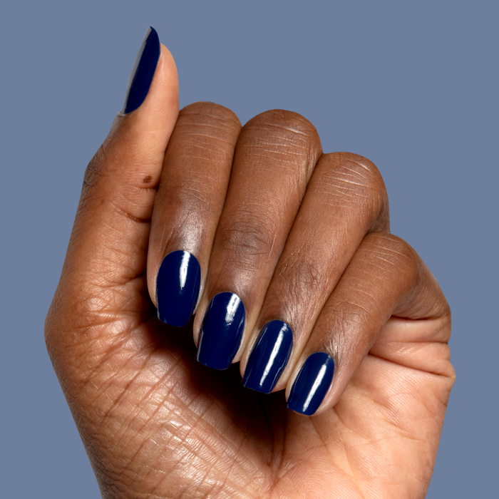 Hand with deep navy blue Power Suit nail polish in glossy finish on medium-length shaped nails against blue background