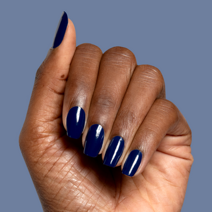 Hand with deep navy blue Power Suit nail polish in glossy finish on medium-length shaped nails against blue background