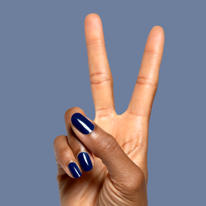 Hand showing peace sign with glossy deep navy blue Power Suit gel polish on neatly shaped nails against blue background