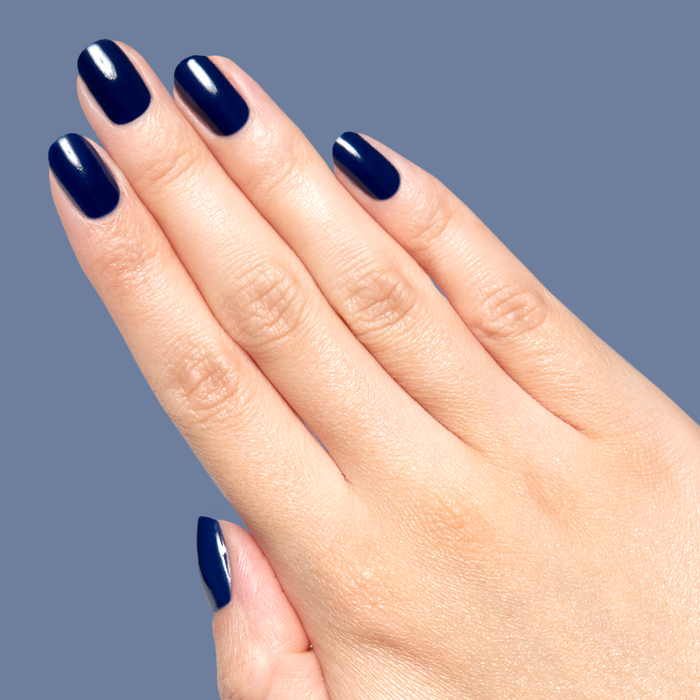 Hand with glossy deep navy blue Power Suit gel polish on short rounded nails against muted blue background