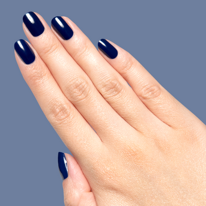Hand with glossy deep navy blue Power Suit gel polish on short rounded nails against muted blue background