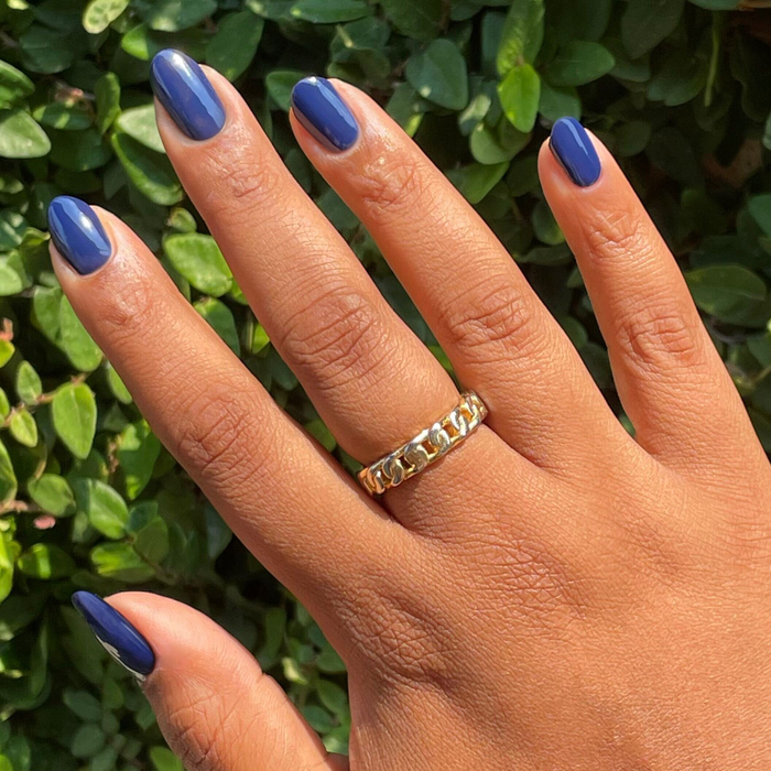 Hand with medium-length deep navy blue Power Suit gel polish on nails against green leafy background