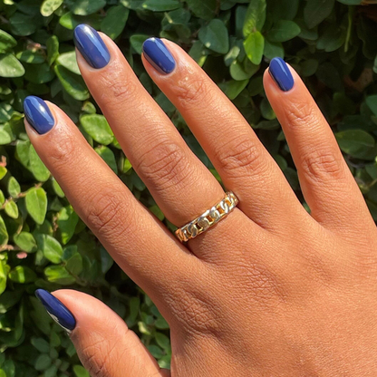 Hand with medium-length deep navy blue Power Suit gel polish on nails against green leafy background